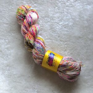 Un écheveau de Sugar Sprinkle, couverts de speckles fuchsia, jaune fluo, bleu et gris, posés sur un fond de fausse fourrure blanche