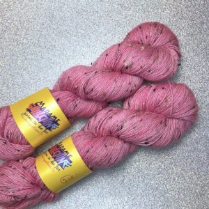 un écheveau de laine rose layette posé sur un fond gris clair à paillettes