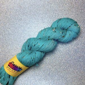 un écheveau de laine tweedée en coloris bleu turquoise posé sur un fond gris clair à paillettes