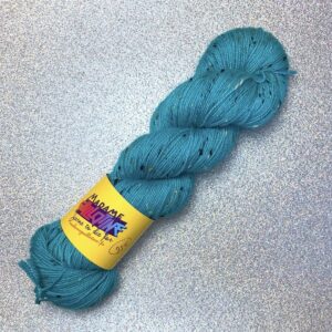 un écheveau de laine bleu turquoise posé sur un fond gris clair à paillettes
