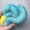 un écheveau de laine tweedée en coloris bleu turquoise posé sur un fond gris clair à paillettes