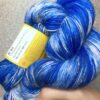 Un écheveau de laine teint à la main dans les tons de bleu électrique varié, posé sur un fond gris clair à paillettes