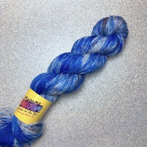 Un écheveau de laine teint à la main dans les tons de bleu électrique varié, posé sur un fond gris clair à paillettes