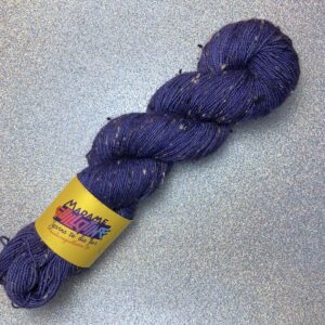 un écheveau de laine violet passé posé sur un fond gris clair à paillettes
