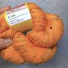 un écheveau de laine orange fluo posé sur un fond gris clair à paillettes