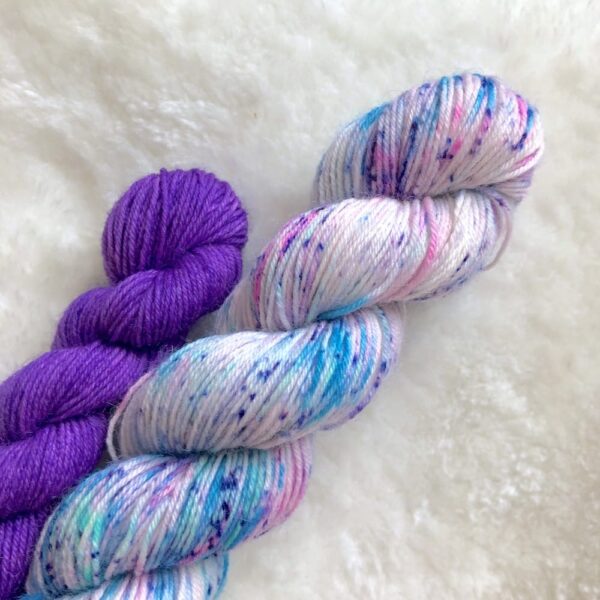 Deux écheveaux de laine teinte à la main, l'un dans les tons de bleu ciel parsemé de speckles violettes et roses et l'autre dans les tons de violet vif
