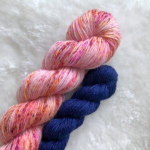 Deux écheveaux de laine teinte à la main, l'un parsemé de speckles rose, rouge et orange et l'autre de couleur unie bleu marine