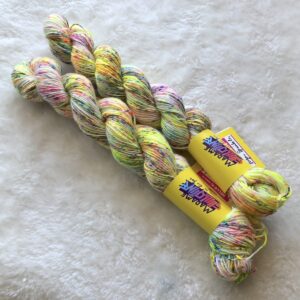 Deux écheveaux de Sugar Sprinkles alignés sur un fond de fausse fourrure blanche, un coloris teint à la main par Madame Guillotine comprenant des speckles jaune et rose fluo et bleu vif