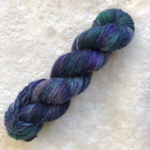 Un écheveau de laine teinte à la main dans des tonalités de violet froid et de vert sapin froid.
