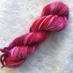 Un écheveau de laine teinte à la main dans les tons de fuchsia, rouge, rose avec des éclats violet.