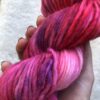 Un écheveau de laine teinte à la main dans les tons de fuchsia, rouge, rose avec des éclats violet.