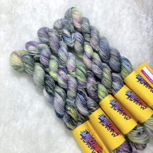 Un écheveau de laine teinte à la main dans des coloris variés de violet et jaune fluo avec des speckles gris métal sur de la fausse fourrure blanche