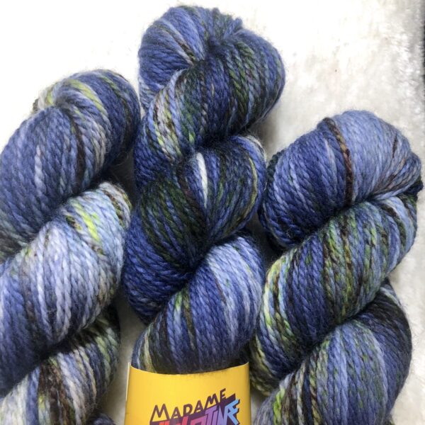 Un écheveau de laine teinte à la main dans des coloris variés de bleu marine, chocolat et vert fluo sur de la fausse fourrure blanche
