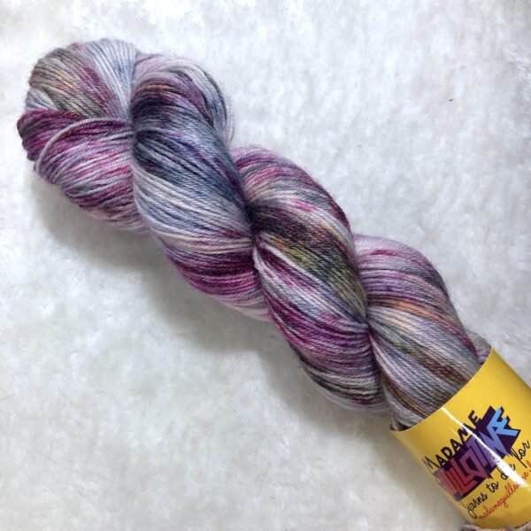 Un écheveau de laine teinte à la main dans des coloris variés de violet et jaune fluo avec des speckles gris métal sur de la fausse fourrure blanche