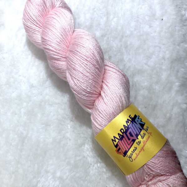 Un écheveau de laine teinte à la main dans un coloris rose très pâle posé sur de la fausse fourrure blanche