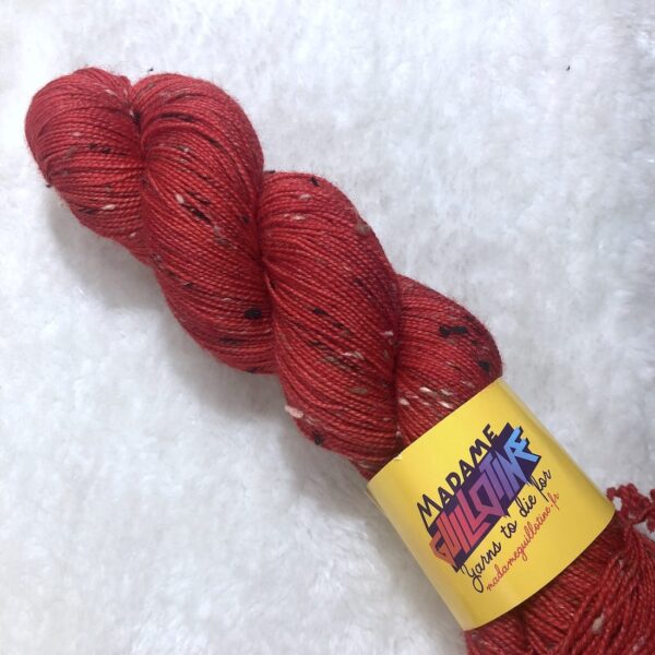 Un écheveau de laine teinte à la main dans un rouge vif posé sur de la fausse fourrure blanche