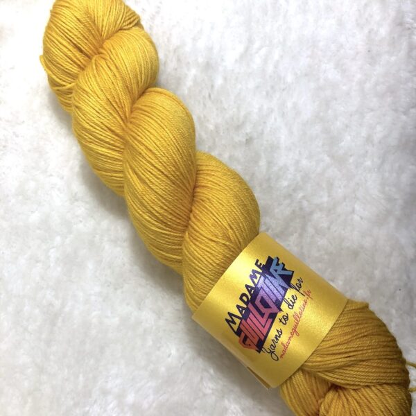 Un écheveau de laine teinte à la main dans un jaune vif posé sur de la fausse fourrure blanche