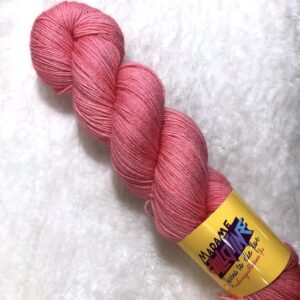 Un écheveau de laine teinte à la main dans un coloris rose vif posé sur de la fausse fourrure blanche